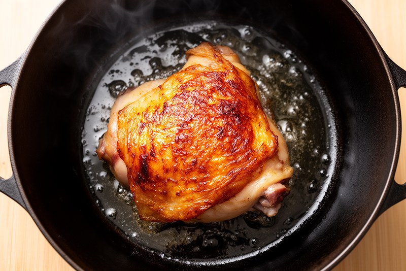 Chicken thigh skin-side down in hot pan developing deep golden-brown crust