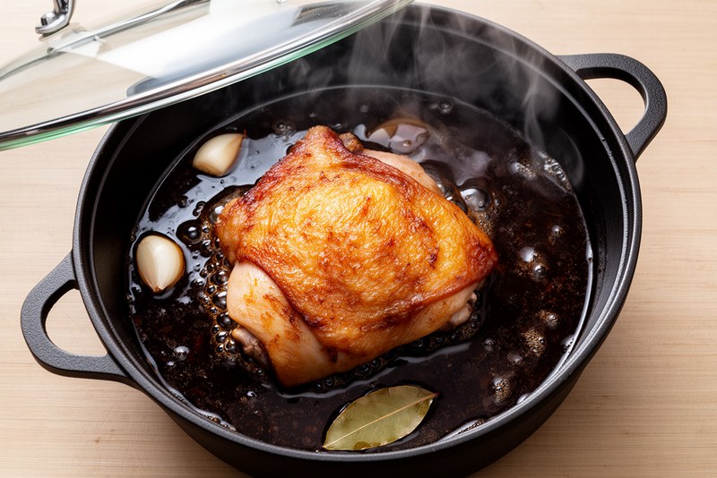 Pot covered with lid, dark adobo sauce simmering gently around bone-in chicken thighs